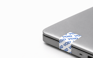 Tamper-evident security labels by JW Products applied to laptop, showing VOID seal for asset tracking and protection