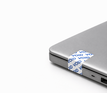 Tamper-evident security labels by JW Products applied to laptop, showing VOID seal for asset tracking and protection