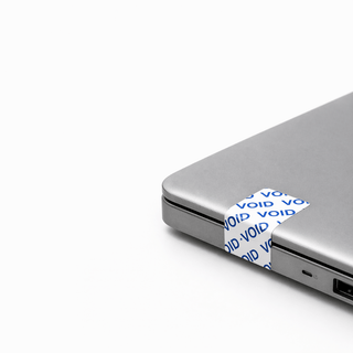 Tamper-evident security labels by JW Products applied to laptop, showing VOID seal for asset tracking and protection