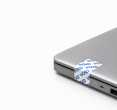 Tamper-evident security labels by JW Products applied to laptop, showing VOID seal for asset tracking and protection