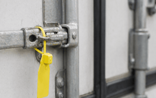 Tamper evident seal from JW Products applied to trailer door latch, showing intact seal for logistics chain of custody and cargo protection