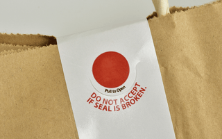 A brown paper bag featuring a prominent red tamper-proof sticker for security and authenticity.