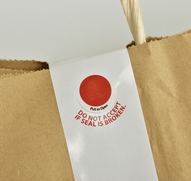 A brown paper bag featuring a prominent red tamper-proof sticker for security and authenticity.
