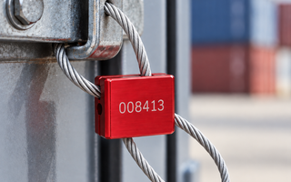 Red numbered cable seal with braided steel wire secured around an industrial metal latch for tamper-evident security and identification.