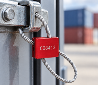 Red numbered cable seal with braided steel wire secured around an industrial metal latch for tamper-evident security and identification.