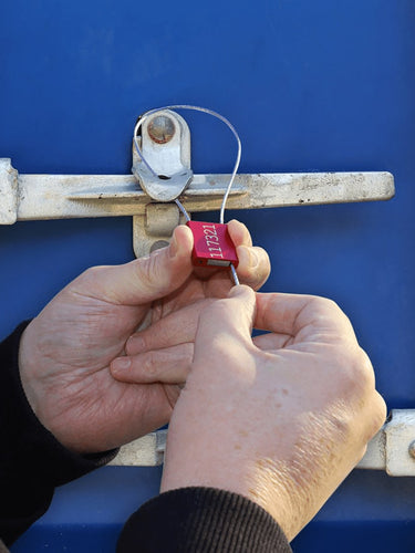 Person using a security seal on a metal latch against a blue background